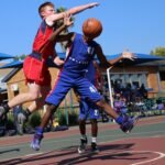 Two athletes playing a competitive basketball game on an outdoor court.